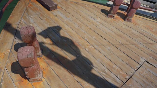 Shadow of waving flag on wooden boat deck on sunny day outdoors at sea. Traditional boat with flag moving in the wind during summer ride in lake or ocean. Jesus tour boat in Sea of Galilee in Israel