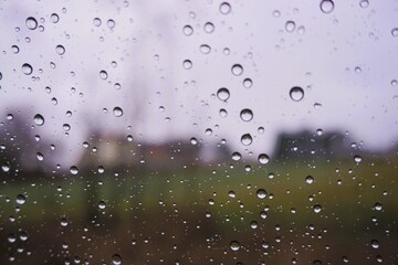 Abstraktes Landschaftspanorama mit Regentropfenmuster vor gr&uuml;ner Wiese mit H&auml;usern und grauem Himmel in der Natur bei Regen, Sturm und K&auml;lte am Nachmittag im Winter