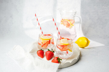 Fresh citrus strawberry drink with lemon slices and ice served in glass on soft towel with whole fruits beside