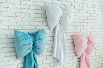 Three large plush bow pillows in blue white and pink hung on a white brick wall