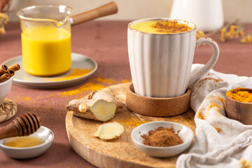 A warm golden milk latte in a white ribbed mug sits on a wooden board surrounded by fresh ginger...