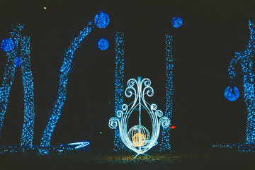 Vibrant blue string lights illuminate trees and an elegant ornamental structure at night, creating a festive display.
