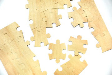 Wooden puzzle pieces rest on a white surface. The pieces are in random order. Some pieces are connected, while others are separate. The scene shows a puzzle-building activity.