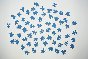Many blue puzzle pieces are mixed on a plain white surface. They are waiting to be sorted and assembled into a complete picture. This activity is engaging and relaxing.