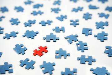 A variety of blue puzzle pieces are spread across a white surface, with one red piece positioned in the center, highlighting how a single element stands out among others