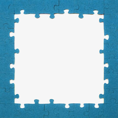 Several blue puzzle pieces are arranged to create a frame on a table. In the center is an empty white space. This setup occurs in a well-lit room during daytime.