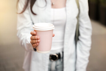 A person stands outside holding a paper cup with a warm drink. They wear simple clothing and enjoy a moment on a city street during the afternoon.