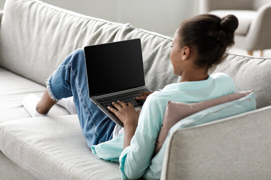 Teen african american girl typing on laptop with empty screen and study at home interior. Female watching online lesson, surfing in internet and chatting in social networks, distance education concept - Powered by Adobe