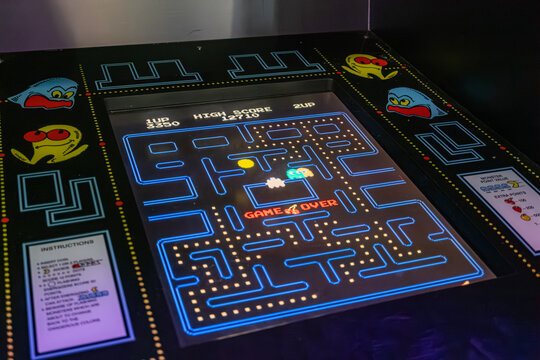 A vintage Pac-Man arcade game machine, illuminated by its own lights, displays the classic game on a colorful screen Buttons for control and text with instructions - Kyiv, Ukraine - June 8, 2025