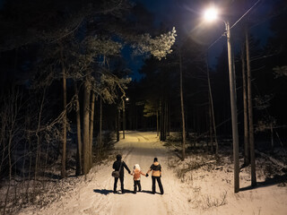 Rear view of a young family with a child holding hands while walking on a snowy road in Estonia winter forest
