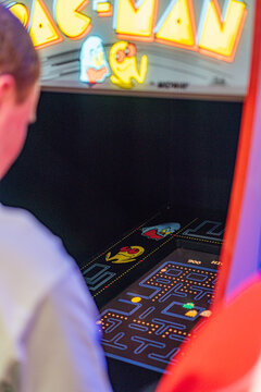 Foreground features a vibrant, red-yellow Pac-Man arcade machine with neon blue lighting A person is playing the game, with the scene viewed from a side angle in an - Kyiv, Ukraine - June 7, 2025