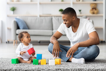 Black Millennial Father And His Adorable Infant Baby Playing With Building Blocks At Home, Young...
