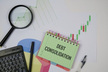 A desk setup featuring a green notebook labeled debt consolidation, a magnifier, charts, and a keyboard, illustrating financial analysis, budgeting, and planning for debt reduction and financial goals
