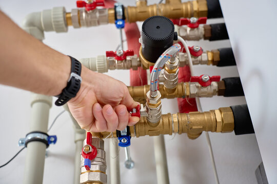 Close-up of technician hand adjusting valve on heat pump piping system with pipes and fittings. Concept of heating maintenance and plumbing service