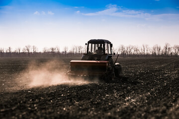 Blue tractor pulling a seed drill machine during spring sowing season. Agricultural landscape with a tractor.