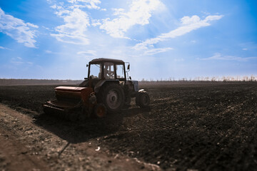 Blue tractor pulling a seed drill machine during spring sowing season. Agricultural landscape with a tractor.
