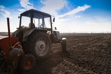Blue tractor pulling a seed drill machine during spring sowing season. Agricultural landscape with a tractor.