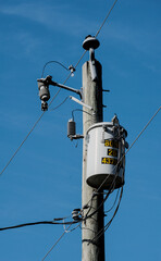 An electrical transformer on a wooden utility pole with power lines under a blue sky in an rural...