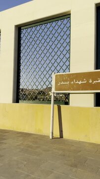 A weathered Arabic signboard for Maqbarat Shuhada Badr, the Cemetery of the Martyrs of Badr, a key historical and religious landmark overlooking the surrounding landscape.