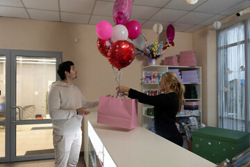 Woman handing pink balloons and gift bag to man in shop
