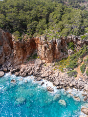 Aerial view of Adrasan, with its calm turquoise waters, a long sandy-pebble beach, and forested mountains in Antalya, Turkey.