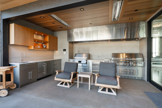 modern fully equipped outdoor kitchen and living area stainless steel appliances cabinetry professional grade grill bbq cooking range exhaust vent hood built in lighting radiant heaters wet bar sink