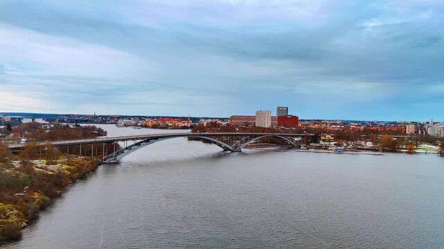 Flying over the peaceful grey waterscape of Lake Malar approaching the large arched Western Bridge. Central part of Stockholm, Sweden at backdrop.