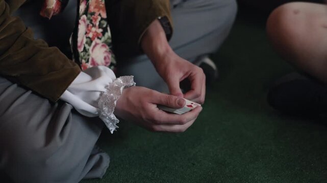 magician performing, card trick, magic show. Magician in theatrical costume performs card trick while seated on floor, showcasing sleight hand and entertainment skills.