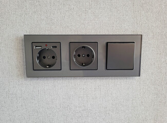 Two sockets and a switch that provide access to electricity on the wall. Electrical sockets for convenient power supply in the office and at home
