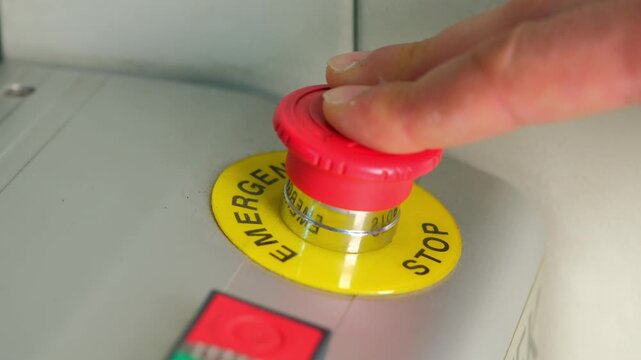 Worker&rsquo;s hand slamming a bright red emergency stop button on an industrial control panel to instantly shut down machinery and prevent accidents in a factory setting