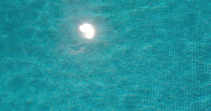 PORTOCOLOM, MALLORCA, SPAIN - OCTOBER, 2025: Gentle ripples move across the surface of a blue swimming pool, sun reflects and dances on the water during a bright relaxing day.