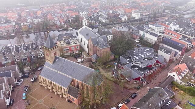 Aerial view of Dutch town gothic church with bell tower, white chapel, canal, and red-roofed homes form a dense, orderly urban layout with historic charm.