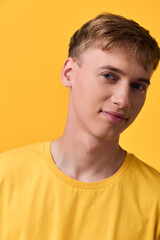 Fototapeta premium Young man in a yellow shirt poses against a vivid yellow backdrop, studio lighting highlighting clean features and a relaxed smile, casual mood perfect for lifestyle and fashion content