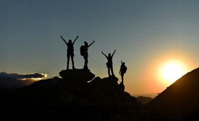 Silhouettes of hikers celebrating success on a mountain peak at sunset. Teamwork, freedom, adventure, and achievement concept.
