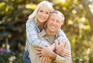 Fototapeta premium Happy elderly man and woman spending time together, embracing, resting in garden at sunny autumn day outdoors and smiling at camera, copy space