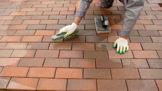 Worker brushing new brick paving during construction