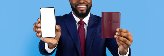 A smiling man in a suit stands against a blue background, holding a smartphone in one hand and a passport in the other. He appears excited and ready for travel.