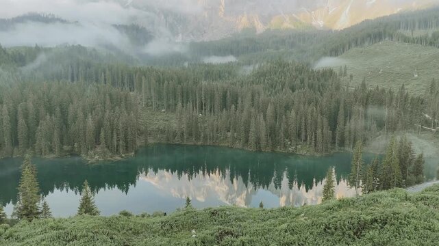Paysage cin&eacute;matographique par drone du Lac de Carezza avec reflet des montagnes et brume matinale, Alpes Italienne