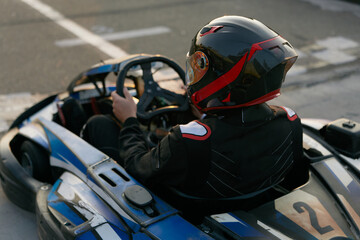 A focused go-kart driver in a sleek helmet prepares to race on a track