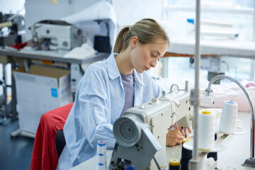 A young seamstress immersed in her craft, diligently focused on sewing in her creative workspace