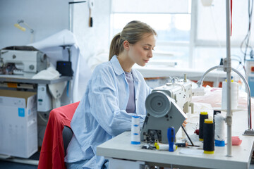 A young seamstress immersed in her craft, diligently focused on sewing in her creative workspace