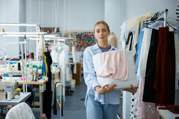 A fashion woman designer in her studio thoughtfully holding different fabrics