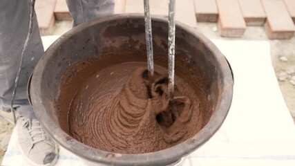 Construction worker preparing fresh mortar in a bucket with an electric mixer, building a new paved walkway outdoors