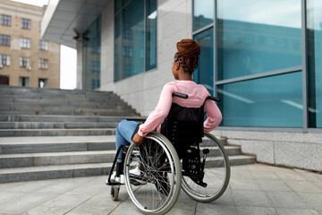 Naklejka premium Disability, environment, mobility and social participation concept. Young black impaired lady in wheelchair cannot go up stairs without ramp, feeling limited and unhappy, copy space