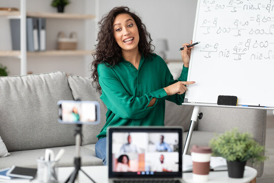 Remote Lecture. Young female teacher explaining math formulas to diverse students, giving online lesson sitting at table, live streaming videochat. Lady recording video blog for her internet channel - Powered by Adobe