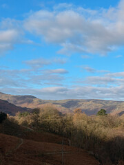 Fototapeta premium Autumn hills and woodland beneath a blue sky with scattered clouds.