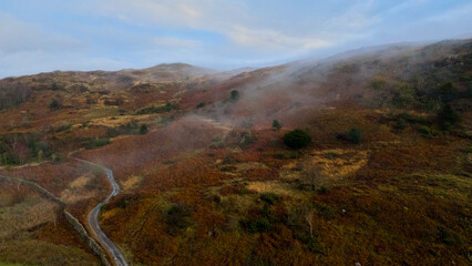 Aerial view of autumn hills with a winding path and drifting fog. © PJSCreativeWorks