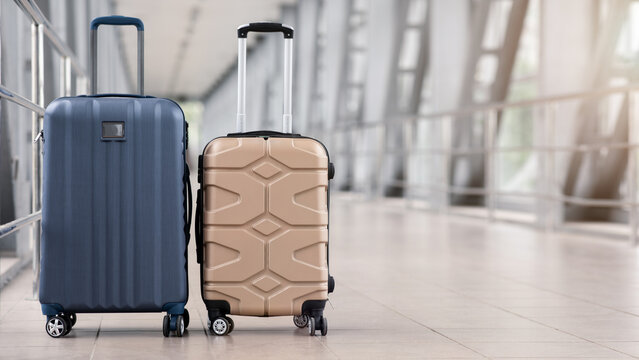 Two stylish suitcases standing in empty airport hall, unrecognizable traveller's luggage waiting in terminal, creative banner for air travels or vacation trip, panorama with copy space