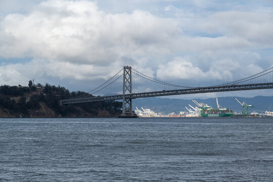 A view of San Francisco looking toward the impressive Bay Bridge leading to Oakland, set beneath an overcast sky that adds a moody, urban atmosphere.