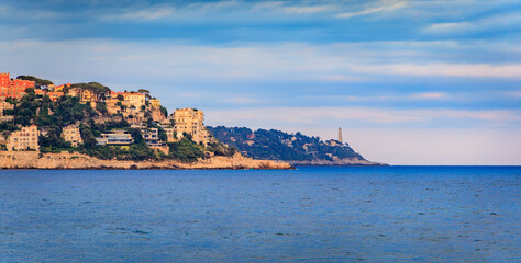 White umbrellas line a pebbled beach under golden sunset clouds in Nice, France